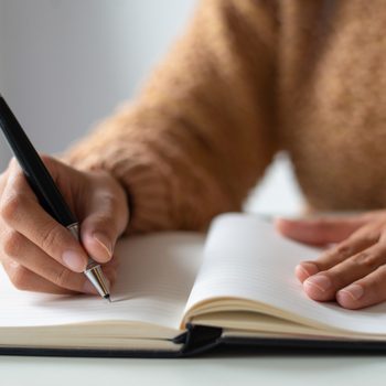 Close-up of businesswoman making notes in personal organizer. Unrecognizable lady writing in diary. Planning time concept