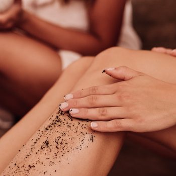 close up of woman applying coffee scrub on leg