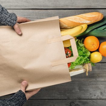 Man's hands holding paper bag of groceries, top view