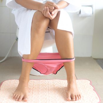 Legs and panties of woman sitting on toilet bowl