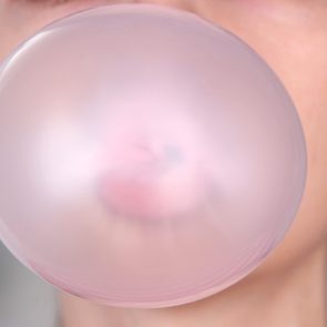 Person doing bubble with chewing gum on bright background