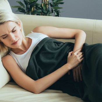 Womsn stomach pain. Female portrait painful girl on sofa bed at home