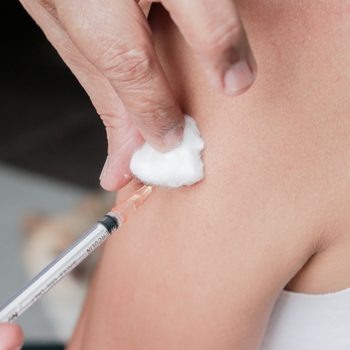 Asian woman is taking vaccine shot on her shoulder.