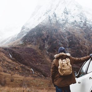 Man driving car on to the mountains. Traveler with backpack. Hiking in cold weather.