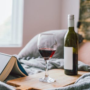 red wine bottle and glass with book on bed