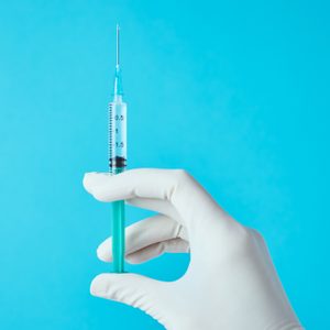 cropped shot of doctor's hand holding vaccine against blue background