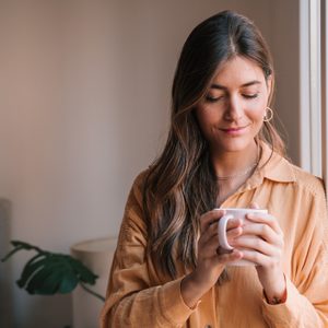 Young Woman Holding Coffee Cup By Window At Home