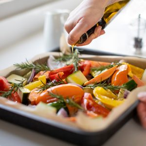 Close Up Of Seasoning Tray Of Vegetables For Roasting With Olive Oil Ready For Vegan Meal