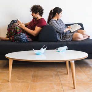 New normal situation after the 2020 coronavirus covid 19 sanitary crisis, a spanish couple rest on a black couch reading books while their surgical masks rest at the living room table