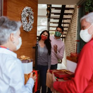 young couple opening front door to grandparents with christmas presents in hands