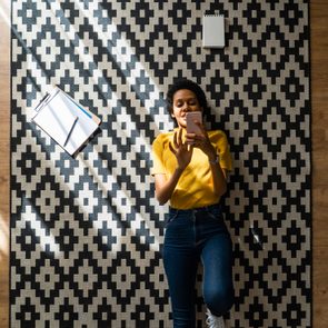 Young woman lying on carpet at home using smartphone