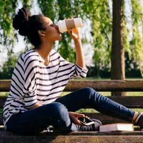 Young woman sitting on park bench drinking coffee to go