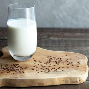 A glass cup of flax milk stands on a wooden board and flax seeds are scattered nearby. Wood background. Healthy snack. Copy space