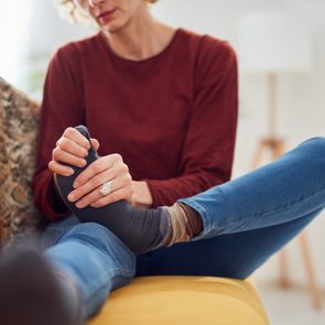 Woman with feet intense pain sitting on a couch at home.