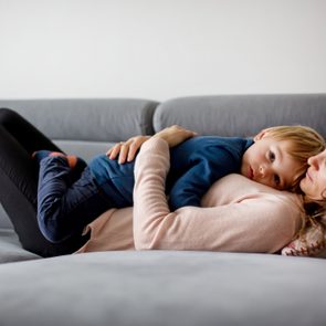 Mother holding sick child, lying together on a couch at home with fever and running nose