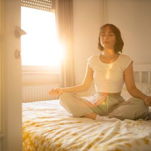 woman practicing meditation in her bed in the morning