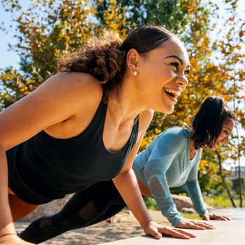 Cheerful women doing push-ups on retaining wall at park