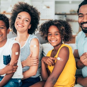 a mother, father, son, and daughter all sitting together showing their bandaids on their arms