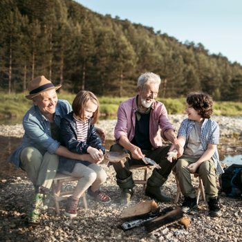 Close up of a multi generation family cooking fish over a campfire outside