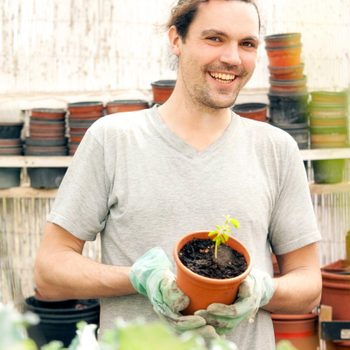 Smiling man holding flowerpot with Moringa seedling