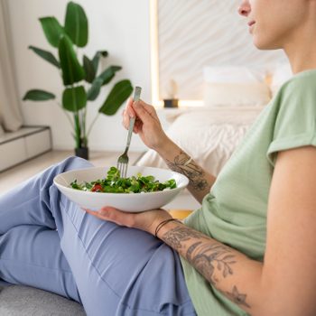 Woman eating salad sitting on sofa at home