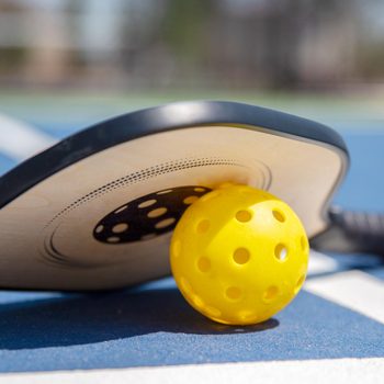 Pickle-ball racket and ball on a court outside